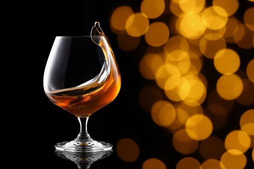 splash of brandy in snifter glass on blurry lights background