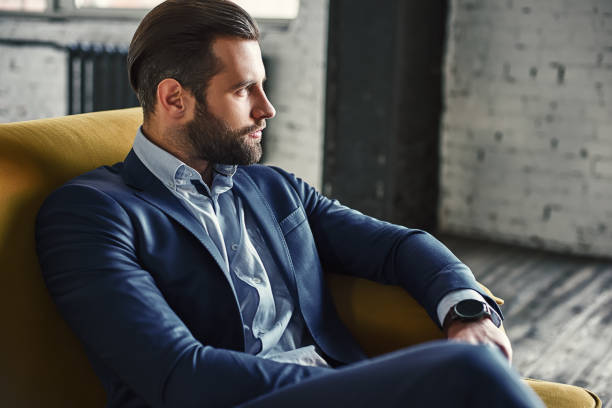 generating ideas...young and charming businessman is thinking about business while sitting on the sofa in his modern office - símbolo sexual imagens e fotografias de stock