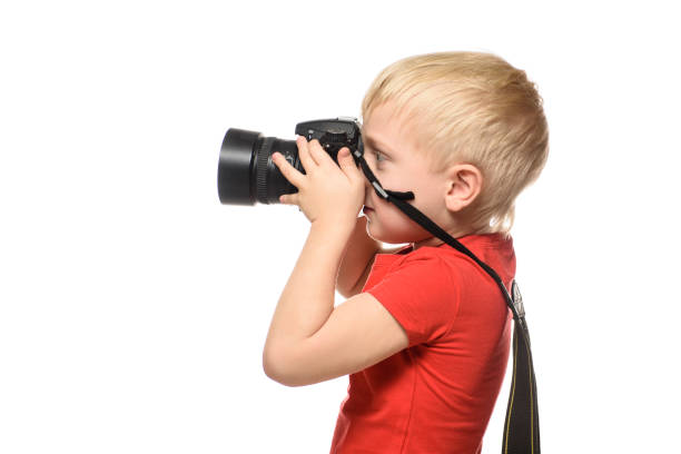 istock Young blond boy in red shirt with camera. Portrait, isolated on white background. Side view. 1127486304
