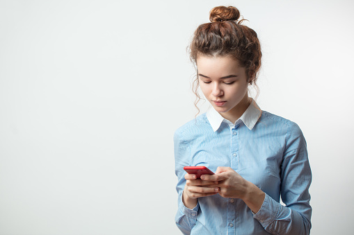 Portrait of an attractive young Caucasian woman in blue shirt using mobile phone on the isolated white background. free time. chat with friends by smartphone