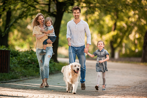 Young smiling family taking their dog for a walk and enjoying in spring day at the park.