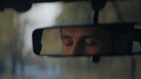 Rear mirror view. Sleepy, tired, fatigued, exhausted young man closing eyes