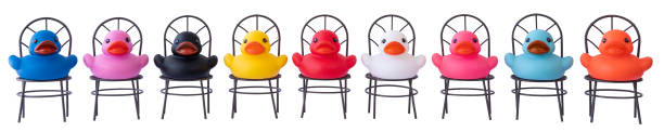 Many different colored rubber ducks sitting on chairs in a row, scene set on a white background. Isolated on white, clipping path included. Concept image regarding multi-ethnic group, togetherness, peace, human rights, social issues etc.