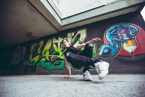 Young man is breakdancing next to graffiti covered wall