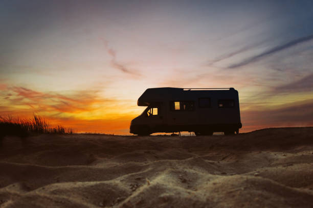 Camper van parked next to beach. Sunset in the background. Summer traveling concept.