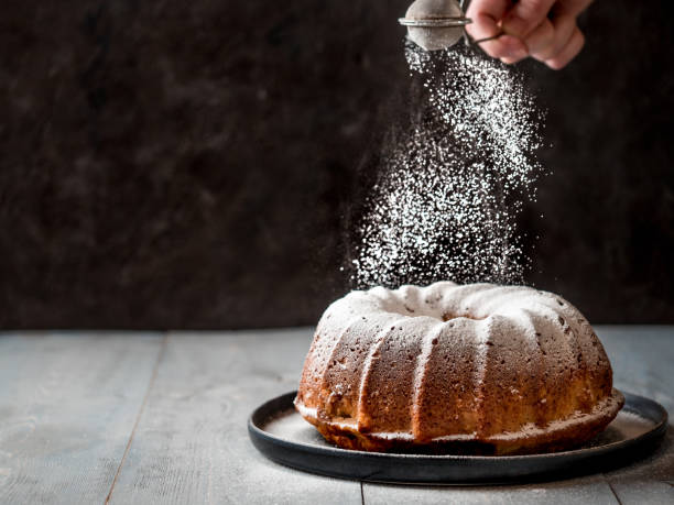 mano femenina rociar azúcar glas en la torta del mollete - espolvorear fotografías e imágenes de stock