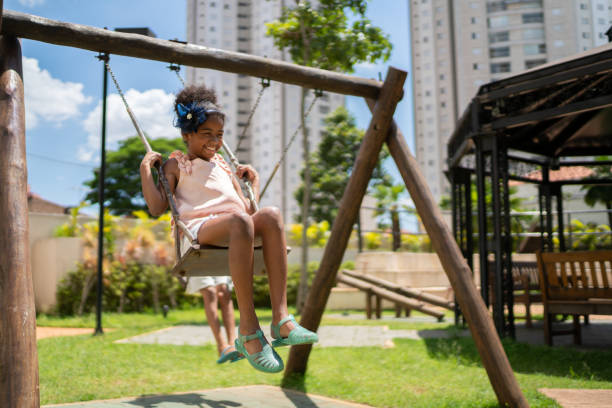 afro latinx children swinging in the playground - playground schoolyard playful playing imagens e fotografias de stock