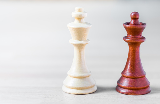 Un rey y una reina de los peones de ajedrez de diverso color de pie lado a lado en una mesa de madera photo