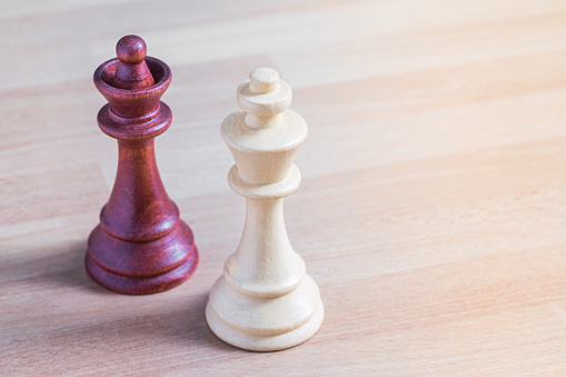 Un rey y una reina de los peones de ajedrez de diverso color de pie lado a lado en una mesa de madera photo