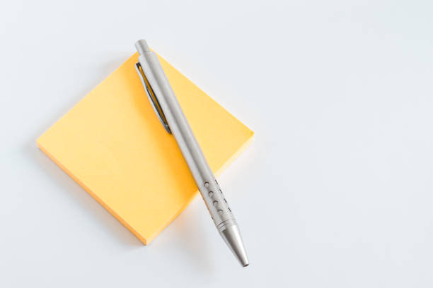 A metal pen on a block of yellow post it on white background A metal pen on a block of yellow post it on white background documento stock pictures, royalty-free photos & images