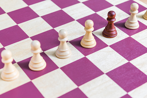 Un peón de ajedrez negro en un tablero de ajedrez alineado con otros peones blancos photo