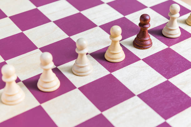 A black chess pawn on a chess board lined up with other white pawns
