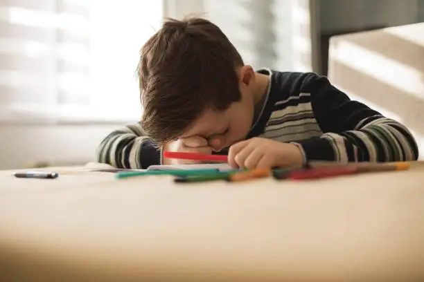 Photo of Tired boy doing his homework at the table