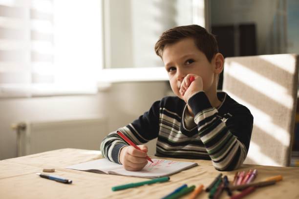 istock Young boy sitting at the table doing his school homework. 1127508015