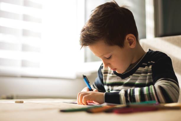 istock Boy at home making homework writing letters with colorful pens 1127508154
