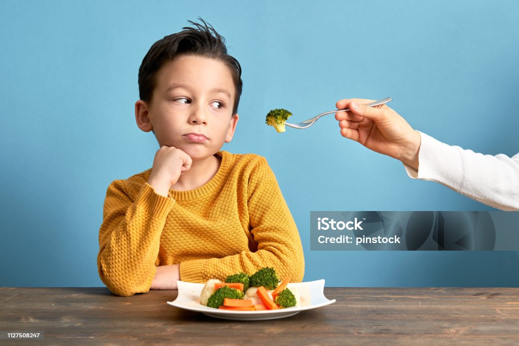 Child is very unhappy with having to eat vegetables. Child is very unhappy with having to eat vegetables. There is a lot of vegetables on his plate. He hates vegetables. Child Stock Photo