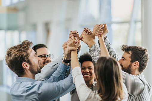 Large group of happy business colleagues holding their hands high up in unity.