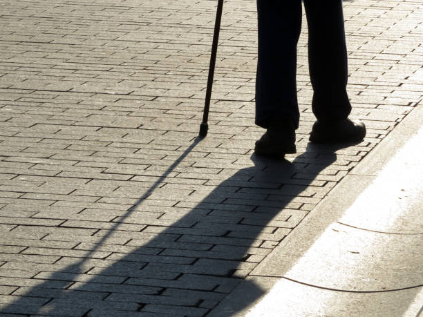 istock Silhouette of man walking with a cane, long shadow on pavement 1127509748