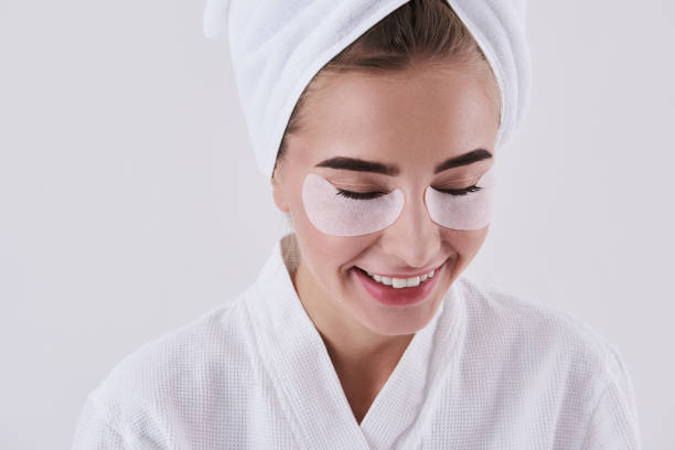 istock Joyful young lady with towel on head using under-eye patches 1127513773