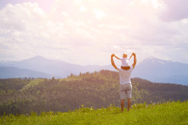 istock Father with a small son on his shoulders. Mountains on the background. Summer sunny day. Back view 1127517490
