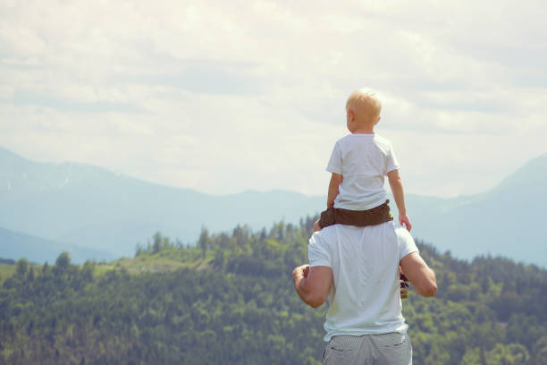 istock Father with a small son on his shoulders. Mountains on the background. Summer sunny day. Back view 1127517492