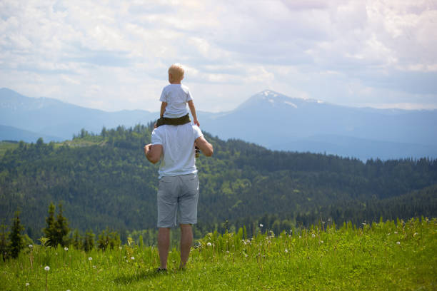 istock Father with a small son on his shoulders. Mountains on the background. Summer sunny day. Back view 1127517497