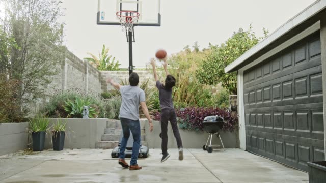 Father and son playing basketball in yard.