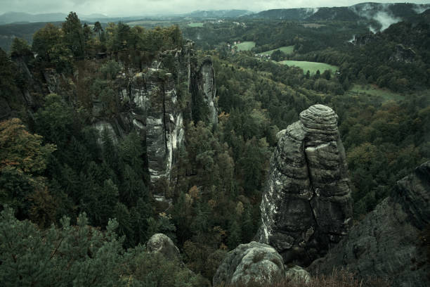 Deadpan dark misty fog mountains from viewpoint of Bastei in Saxon Switzerland, Germany to the mountains at sunrise in the morning fog, National park Saxon Switzerland Deadpan dark misty fog mountains from viewpoint of Bastei in Saxon Switzerland, Germany to the mountains at sunrise in the morning fog, National park Saxon Switzerland. pravcicka stock pictures, royalty-free photos & images