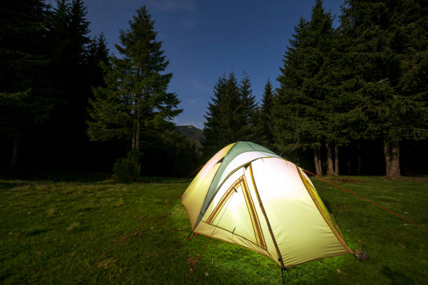 istock Summer camping at night. Illuminated tourist tent on green clearing on distant mountain background. 1127524483