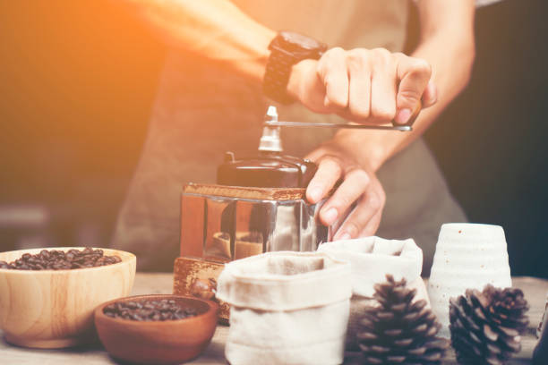 Barista is grinding coffee with a hand coffee grinder.