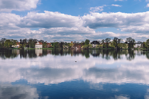 Traditional german houses, mansions rand clouds eflected on the water of Heiliger See lake in Potsdam, Germany. View from New Garden park bank.
