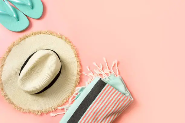 Female outfit for beach. Straw sunhat and beach slaps on punchy pink with space for text. Summer tropical concept.