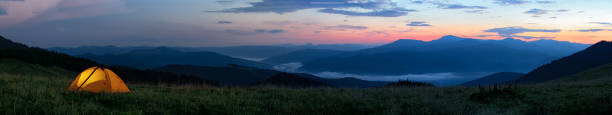 istock Orange tourist tent illuminated from inside stands in mountains above clouds 1127529873