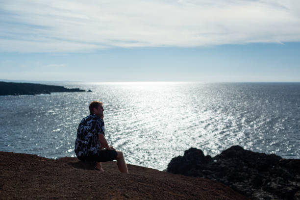 istock A man looks at the sea, sitting on a stone. 1127530754