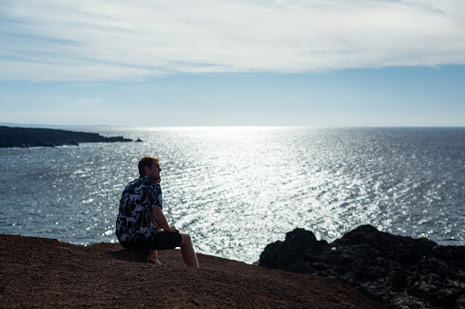 A man looks at the sea, sitting on a stone. The famous beach of El Golfo, Lanzarote.