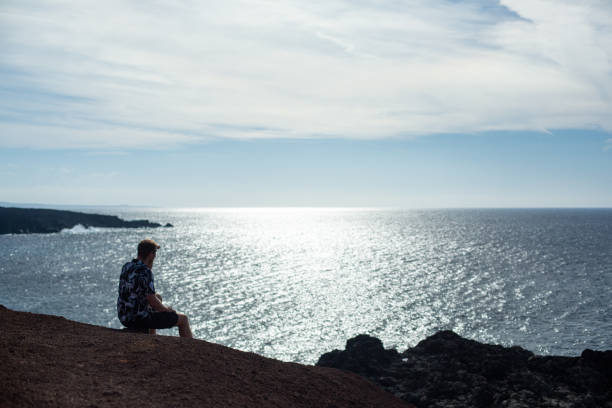 istock A man looks at the sea, sitting on a stone. 1127530759