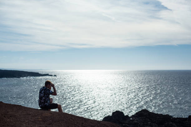 istock A man looks at the sea, sitting on a stone. 1127530760
