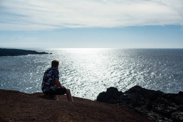 istock A man looks at the sea, sitting on a stone. 1127530762