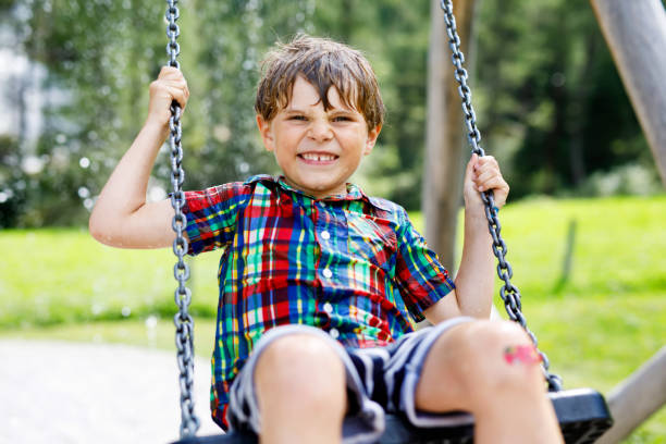 istock Funny kid boy having fun with chain swing on outdoor playground while being wet splashed with water. child swinging on summer day. Active leisure with kids. Happy crying boy with rain drops on face. 1127535444