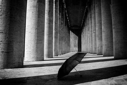 An umbrella abandoned on the ground in the shadow of a black and white colonnade