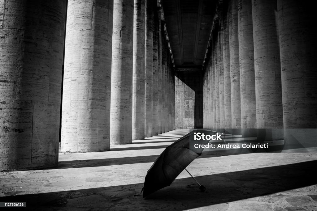 An umbrella abandoned on the ground in the shadow of a black and white colonnade Autumn Stock Photo