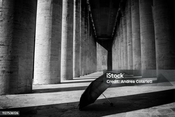 An Umbrella Abandoned On The Ground In The Shadow Of A Black And White Colonnade Stock Photo - Download Image Now