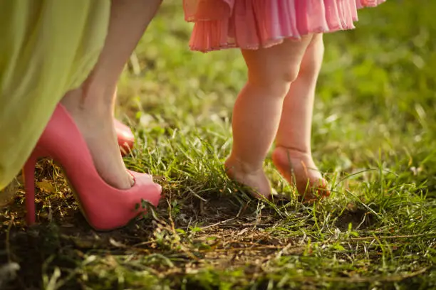 Mother's legs in shoes with the high heels and daughter with the barefoot. Photo was made in summer on a green grass