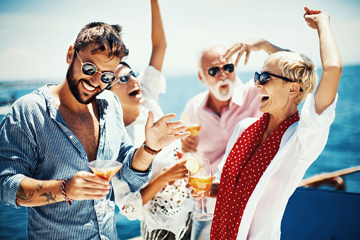 Group of people dancing at yacht party. They are holding cocktails and raising their arms. They enjoying and having fun.