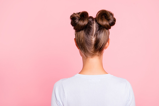 Rear back behind view of nice attractive groomed girl wearing two fashionable buns isolated over pink pastel background