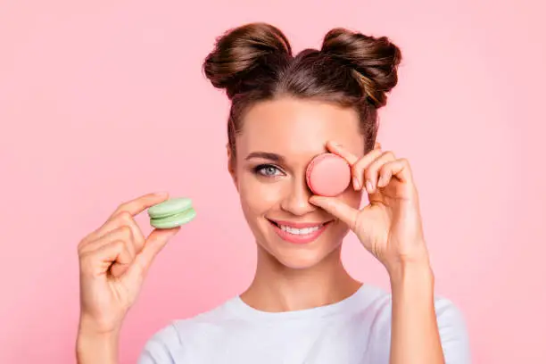 Photo of Close-up view of nice attractive funny girlish cheerful girl closing one eye with sugary colorful yummy tasty delicious pies confection isolated over pink background