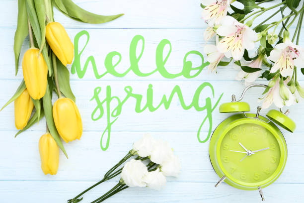 istock Fresh flowers with text Hello Spring and alarm clock on wooden table 1127542242