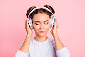 Close-up portrait of nice lovely sweet attractive calm peaceful conecnrated focused girl wearing touching earphones closed eyes isolated over pink pastel background
