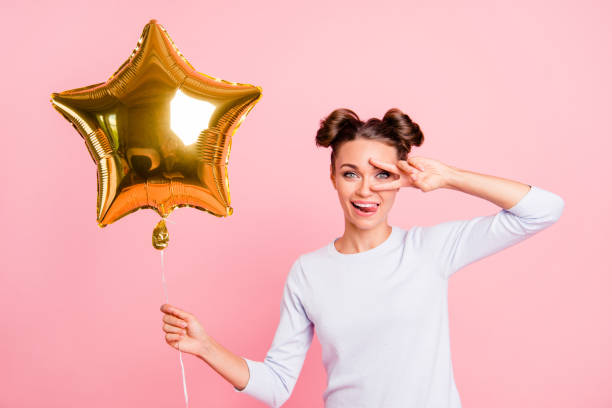 Portrait of nice cute adorable attractive lovely cheerful cheery positive funny funky girl holding big air baloon golden star showing v-sign isolated over pastel pink background Portrait of nice cute adorable attractive lovely cheerful cheery positive funny funky girl holding big air baloon golden star showing v-sign isolated over pastel pink background topknot stock pictures, royalty-free photos & images