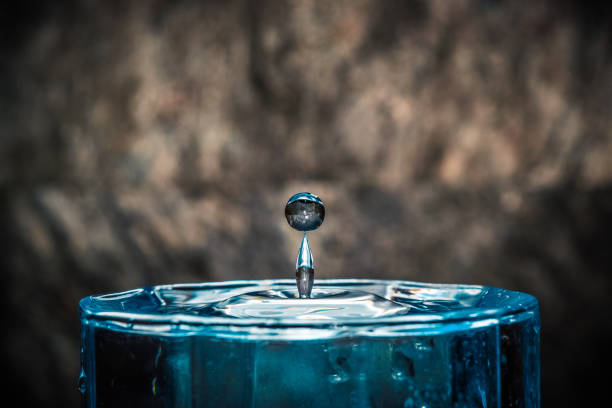 A drop of water falls into a glass of squared glass A drop of water falls into a glass of squared glass bicchiere stock pictures, royalty-free photos & images